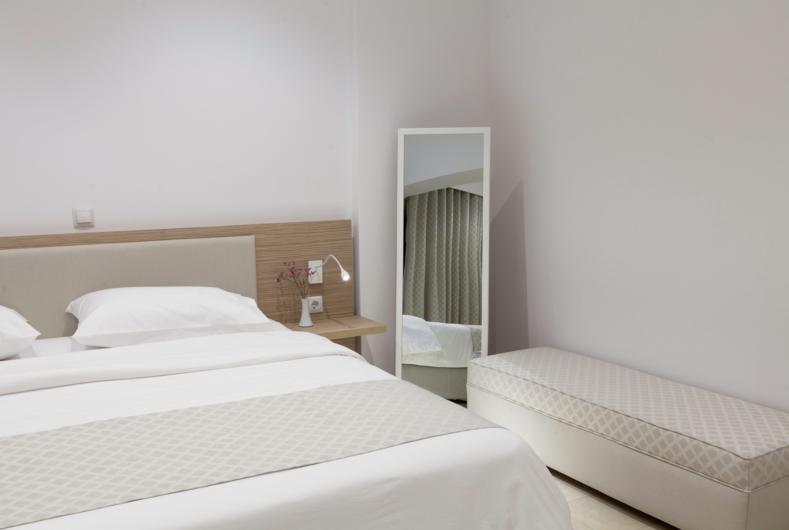 A hotel room with a large bed, a bedside table with a lamp, and a mirror.