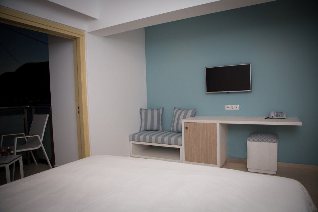 A bedroom with a bed, a desk with a chair, a TV mounted on the wall, and a small cabinet.