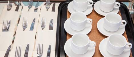 A tray with white cups and saucers, arranged neatly on a corkboard surface.