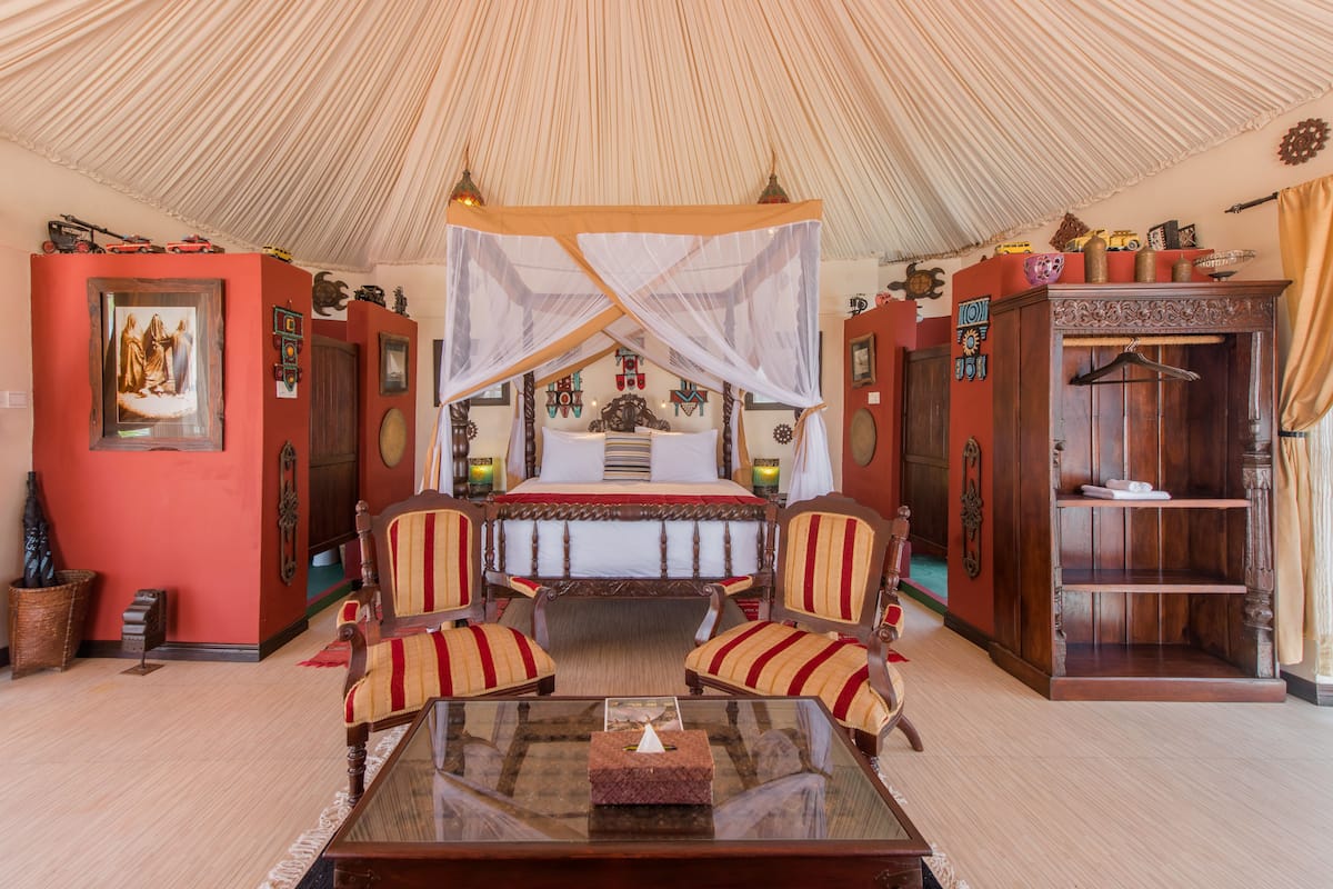 A room with a canopy bed, striped armchairs, a wooden cabinet, and a glass coffee table.
