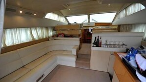 A yacht interior with a curved seating area, a small kitchenette, and a window providing natural light. - Raxul Boat (Villasimius)