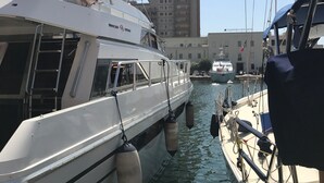 A marina with boats docked, including a white yacht with a covered deck and a building in the background. - Raxul Boat (Villasimius)