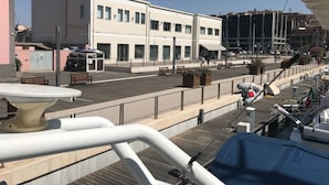 A waterfront promenade with a white building, benches, and a marina with boats. - Raxul Boat (Villasimius)
