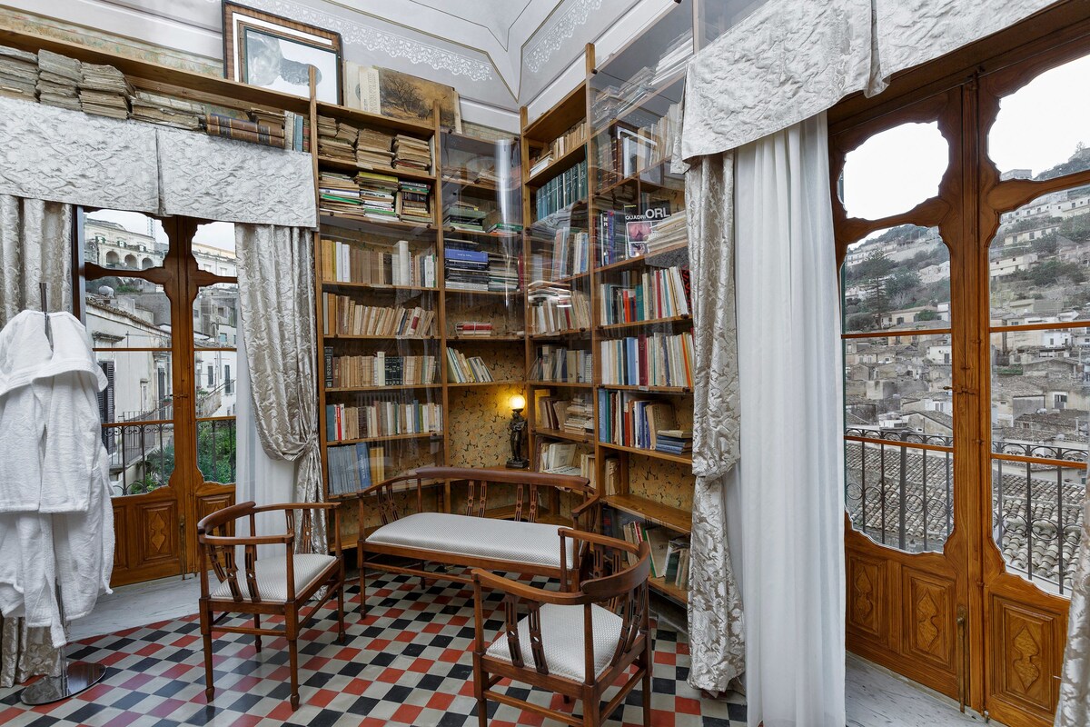 Une bibliothèque avec des étagères, un banc en bois et une vue sur les bâtiments par une fenêtre.