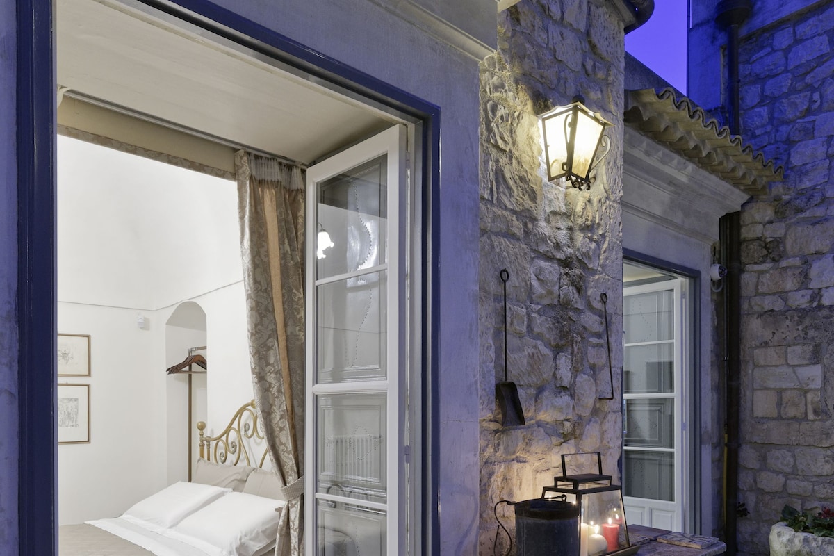 Une pièce avec un lit, un pilier en pierre surmonté d’une lanterne et une fenêtre avec des rideaux.