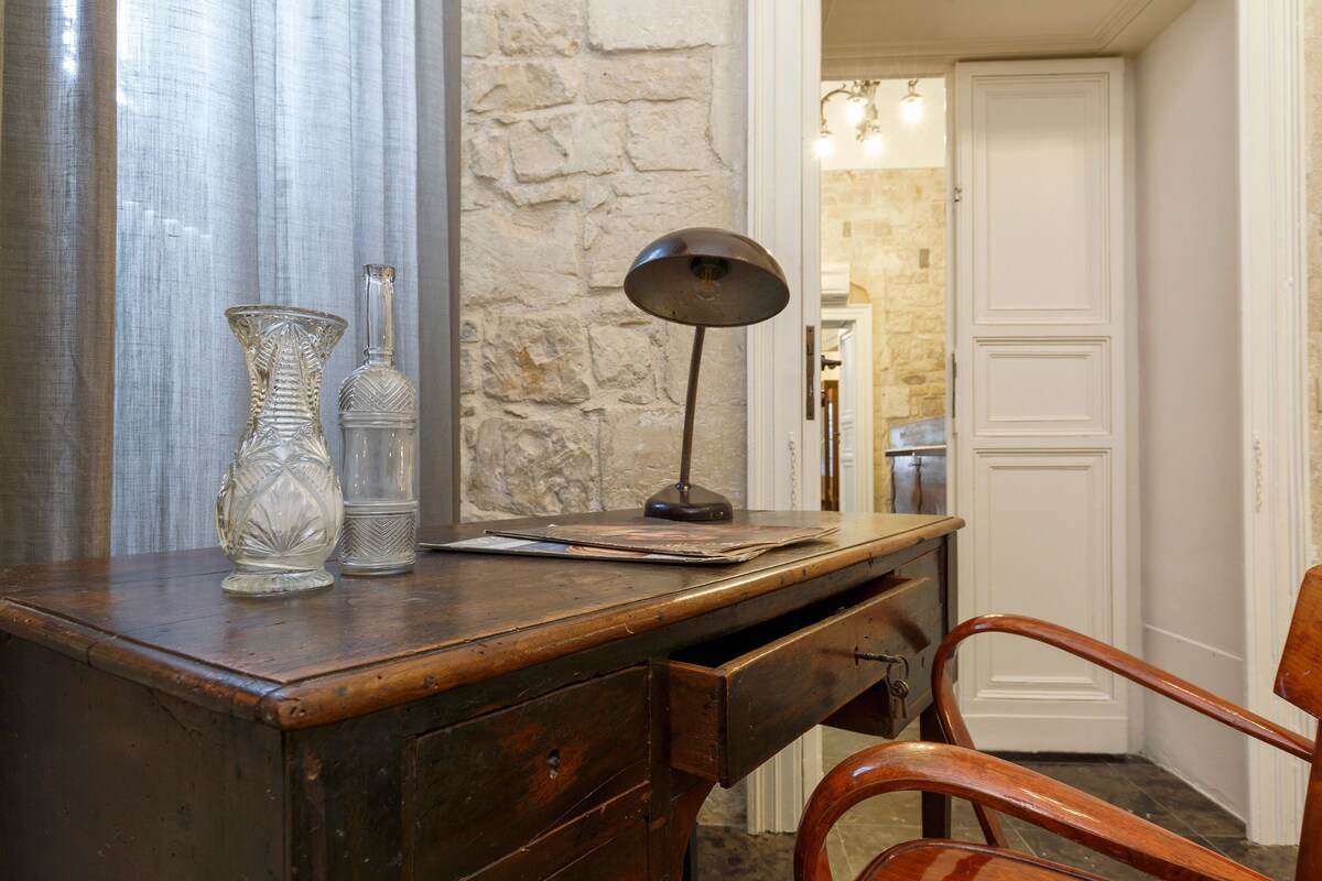 Un bureau en bois, orné de deux vases en verre, d’une lampe et d’un carnet.