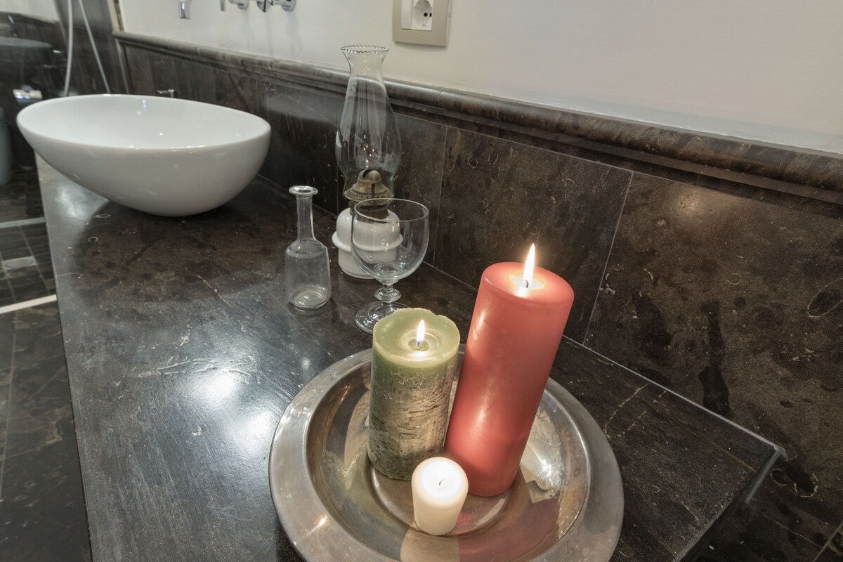 Un meuble-lavabo de salle de bain avec un évier blanc, un vase en verre, une bougie et un petit flacon en verre.