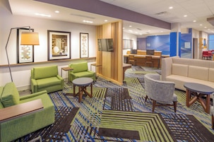 Un vestíbulo de hotel con asientos verdes, un televisor y una alfombra estampada.