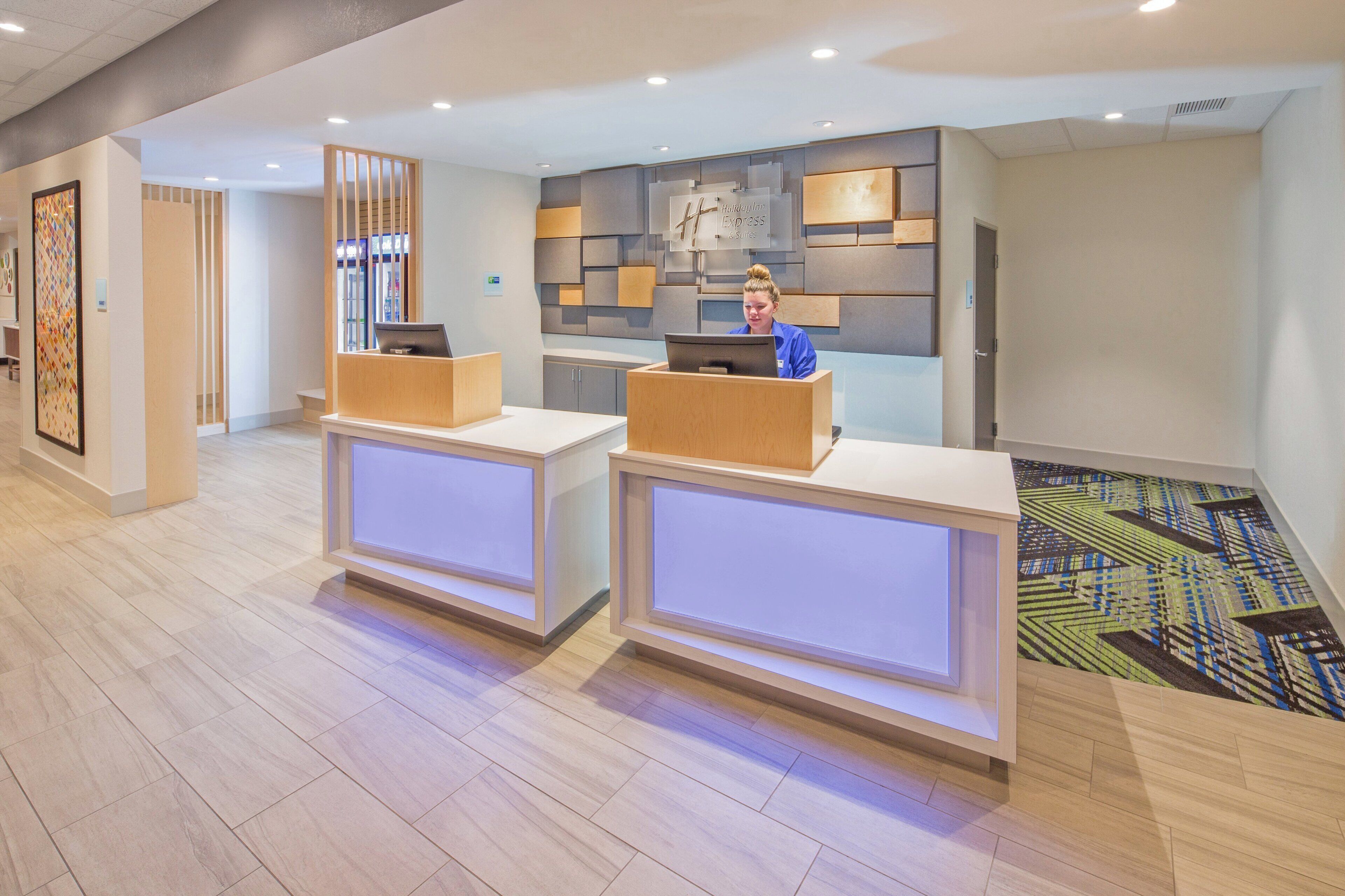 A hotel reception area with two reception desks, a decorative wall, and a patterned carpet.