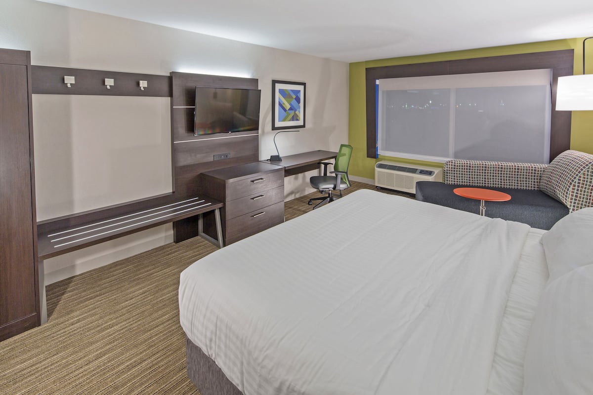 Een hotelkamer met een groot bed, een bureau met stoel, een televisie en een raam met uitzicht op de stad.