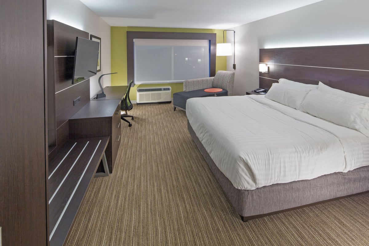 Hotelkamer met een groot bed, een bureau, een flatscreen televisie, een stoel en een raam met jaloezieën.