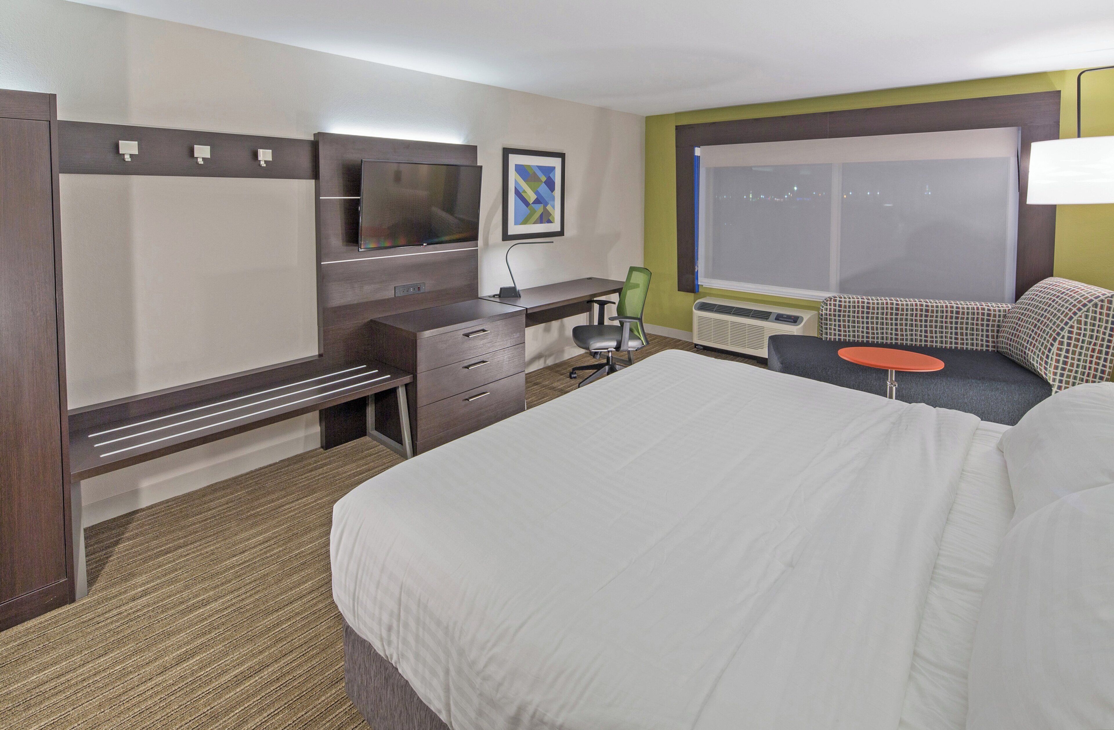 Una habitación de hotel con una cama, un escritorio, una silla, un televisor y una ventana con vistas.