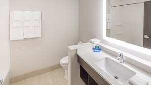 A modern bathroom with a white sink, mirror, and toilet. There are white towels hanging on the wall and a small blue bottle on the counter. - Holiday Inn Express & Suites Indianapolis NW - Zionsville by IHG (Whitestown)