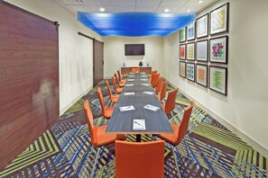 Un salón de conferencias con una larga mesa, sillas anaranjadas, alfombra estampada y cuadros en las paredes.