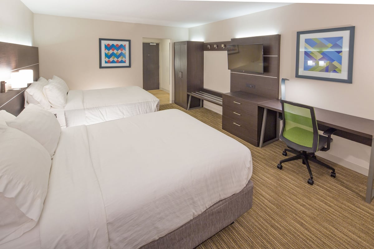 Een hotelkamer met twee bedden, een bureau, een stoel, een televisie en kunstwerken aan de muur.