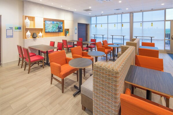 A hotel lobby with multiple seating areas, a television mounted on the wall, and large windows providing a view of the outdoors. - Holiday Inn Express & Suites Indianapolis NW - Zionsville by IHG (Whitestown)