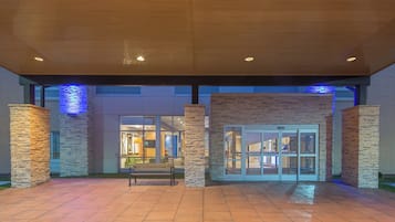 A covered outdoor area with stone pillars, a bench, and a building entrance with glass doors.