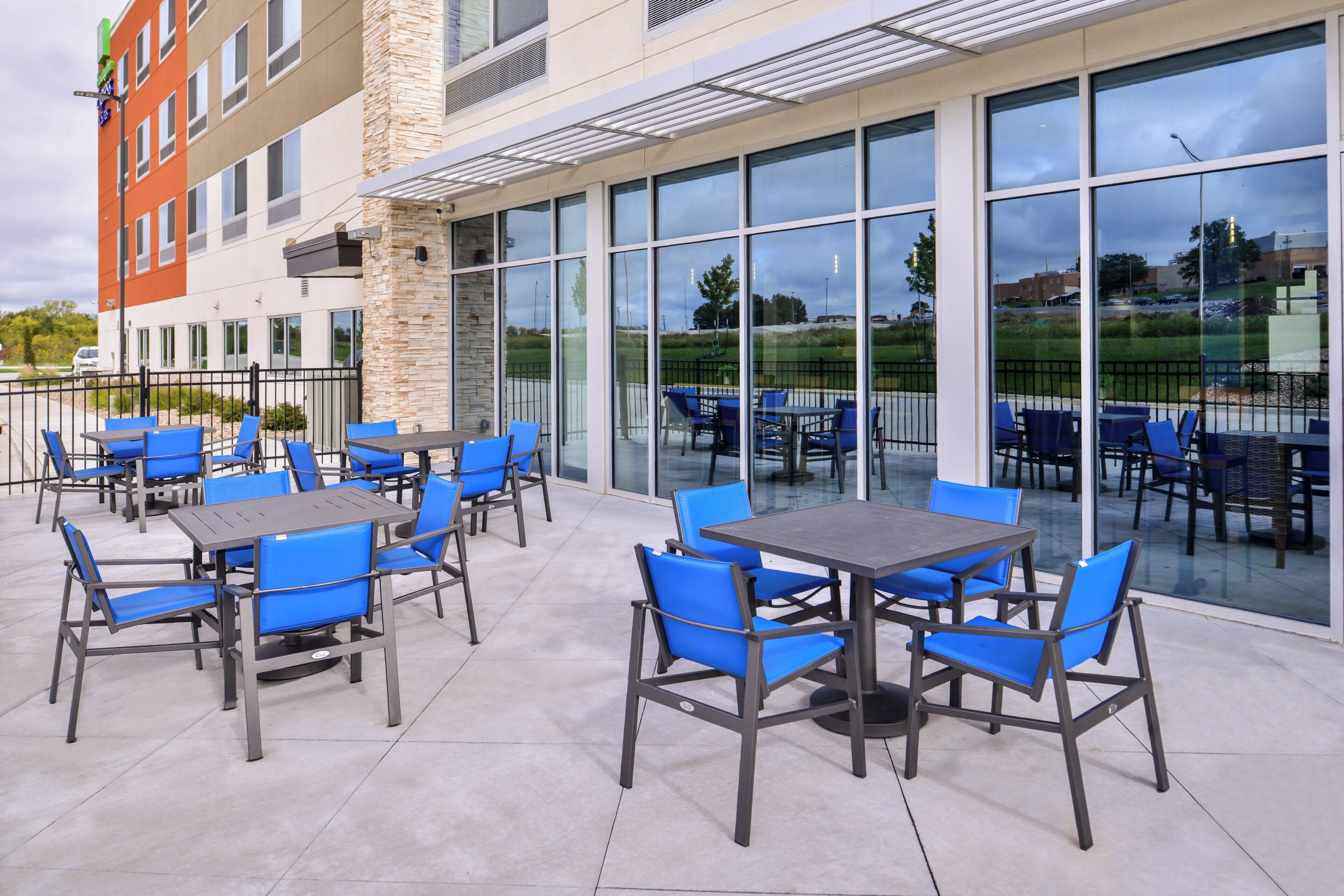 Un espace extérieur aménagé en terrasse, avec des tables et des chaises, de grandes fenêtres et une vue sur les environs.