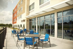 An outdoor patio area with tables and chairs, large windows, and a building with a brick facade. - Holiday Inn Express & Suites Kansas City - Lee's Summit by IHG (Lee's Summit)