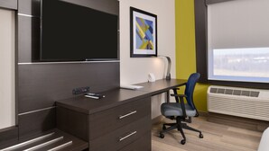 A modern office space with a dark brown desk, a flat-screen TV, a framed abstract art piece, and a window with blinds. - Holiday Inn Express & Suites Kansas City - Lee's Summit by IHG (Lee's Summit)