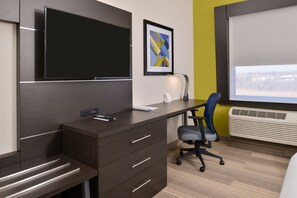 A modern office space with a dark brown desk, a flat-screen TV, a framed abstract art piece, and a window with blinds. - Holiday Inn Express & Suites Kansas City - Lee's Summit by IHG (Lee's Summit)