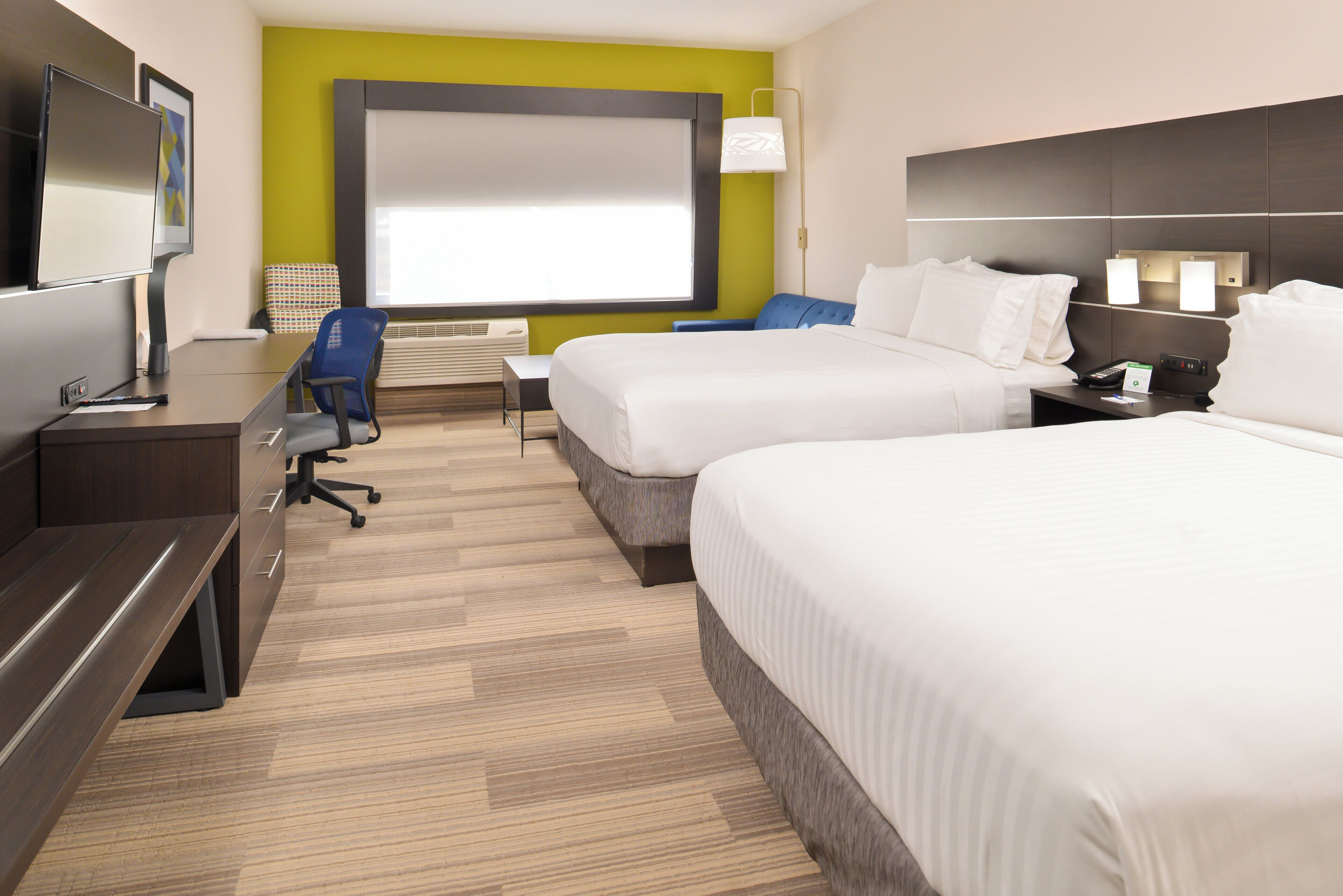 A hotel room with two beds, a desk, a chair, a TV, and a window with blinds.