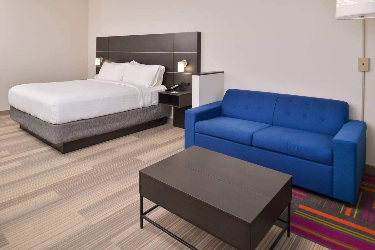 A hotel room with a bed, a blue sofa, a small table, and a nightstand with a lamp.