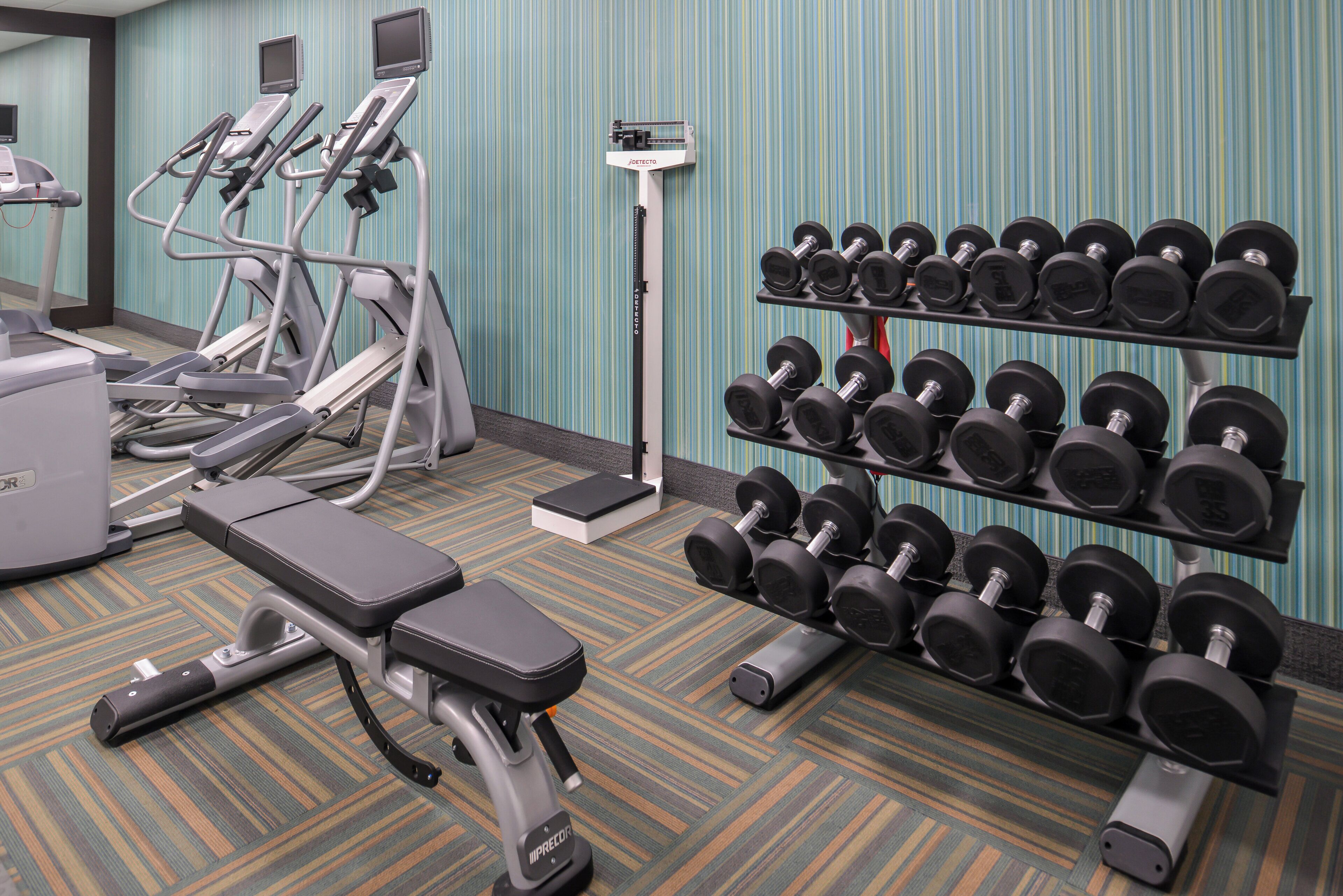 Une salle de sport équipée de matériel d’exercice, notamment des tapis de course, un banc et un porte-haltères.