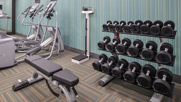 Une salle de sport équipée de matériel d’exercice, notamment des tapis de course, un banc et un porte-haltères.