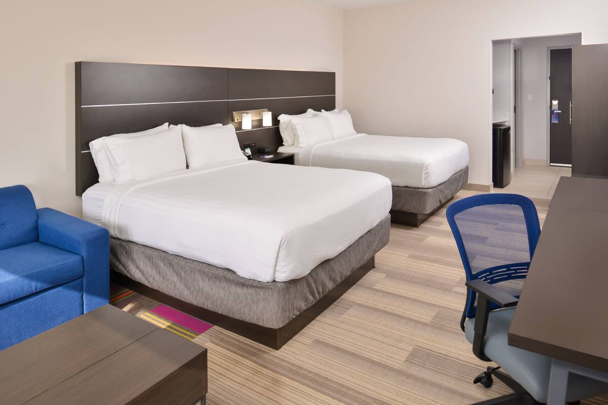 A hotel room with two beds, a desk, a chair, and a blue sofa.