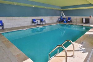 Una piscina con un borde de baldosas, un puesto de salvavidas y sillas reclinables azules.