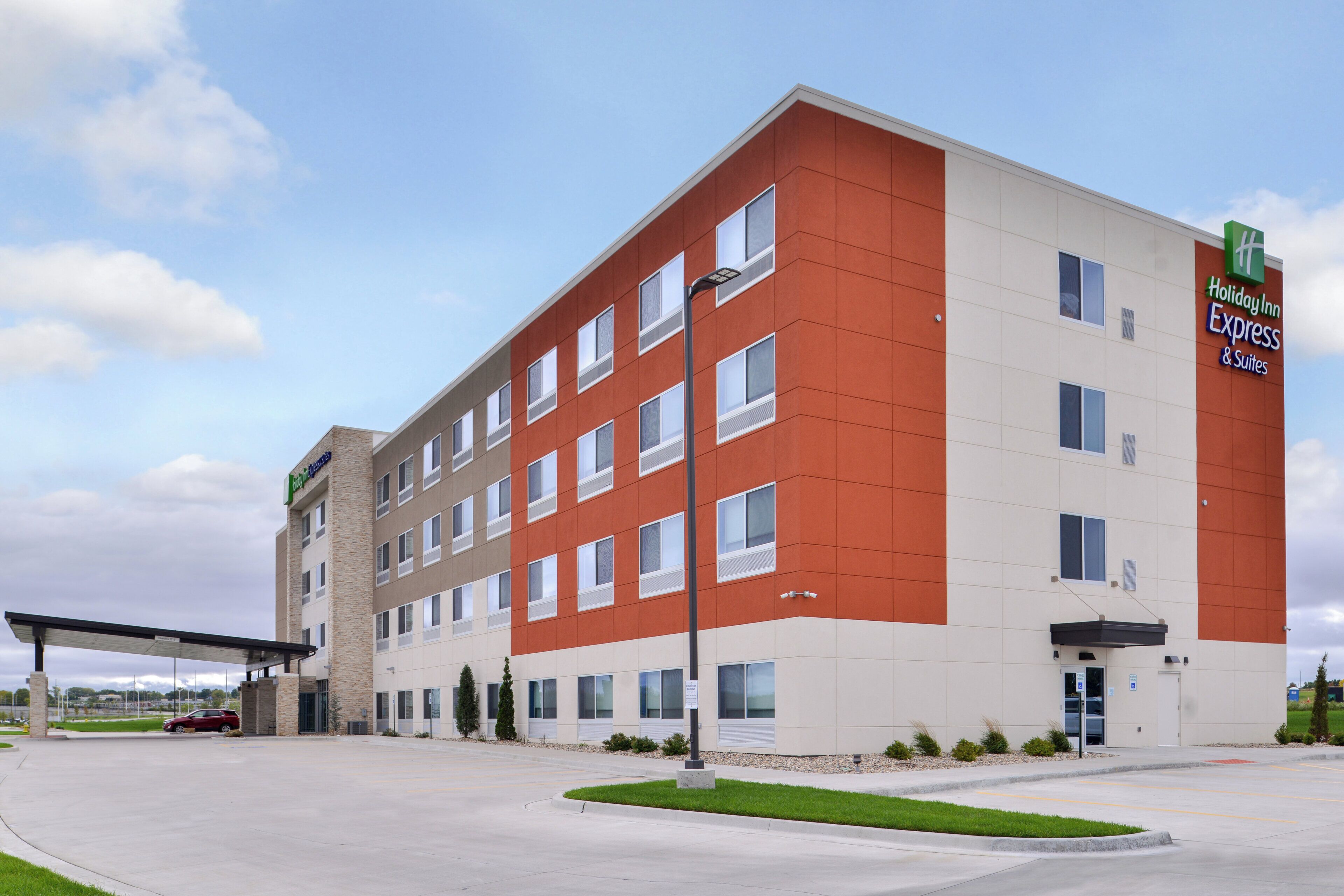 Ein Hotel Holiday Inn Express & Suites mit modernem Design, das ein flaches Dach und eine Kombination aus Beige- und Rottönen an der Außenfassade aufweist.