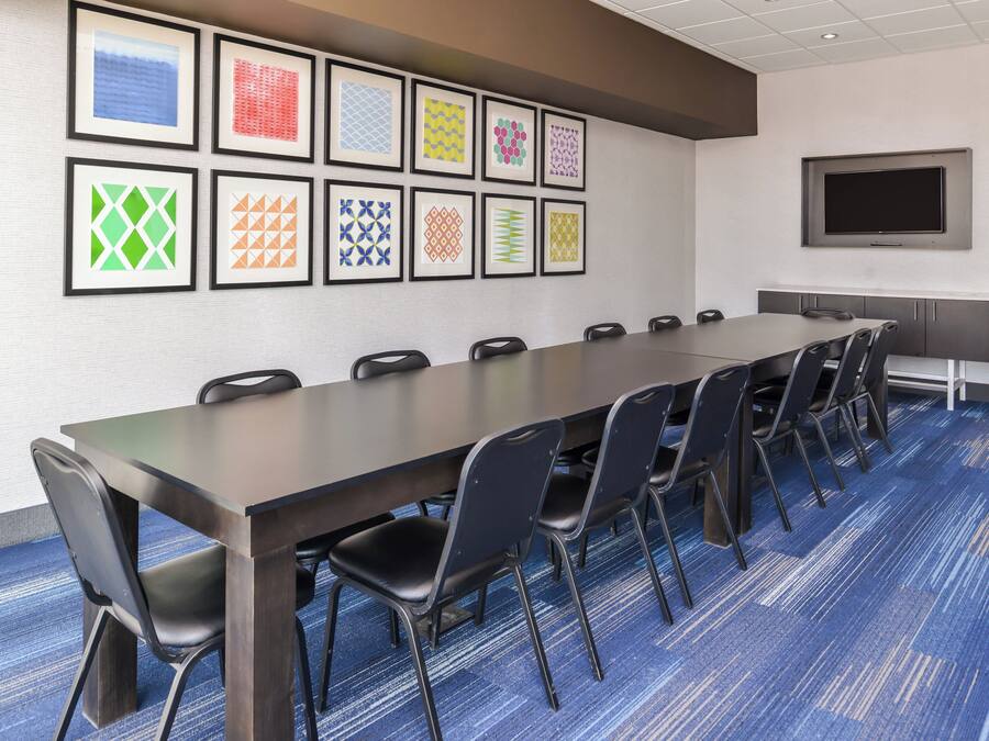 A conference room with a long table, chairs, a flat-screen TV, and framed artwork on the wall.