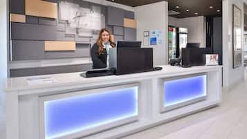 Un mostrador de recepción de hotel con un diseño moderno, que incluye un monitor de pantalla plana, una computadora y una caja registradora.