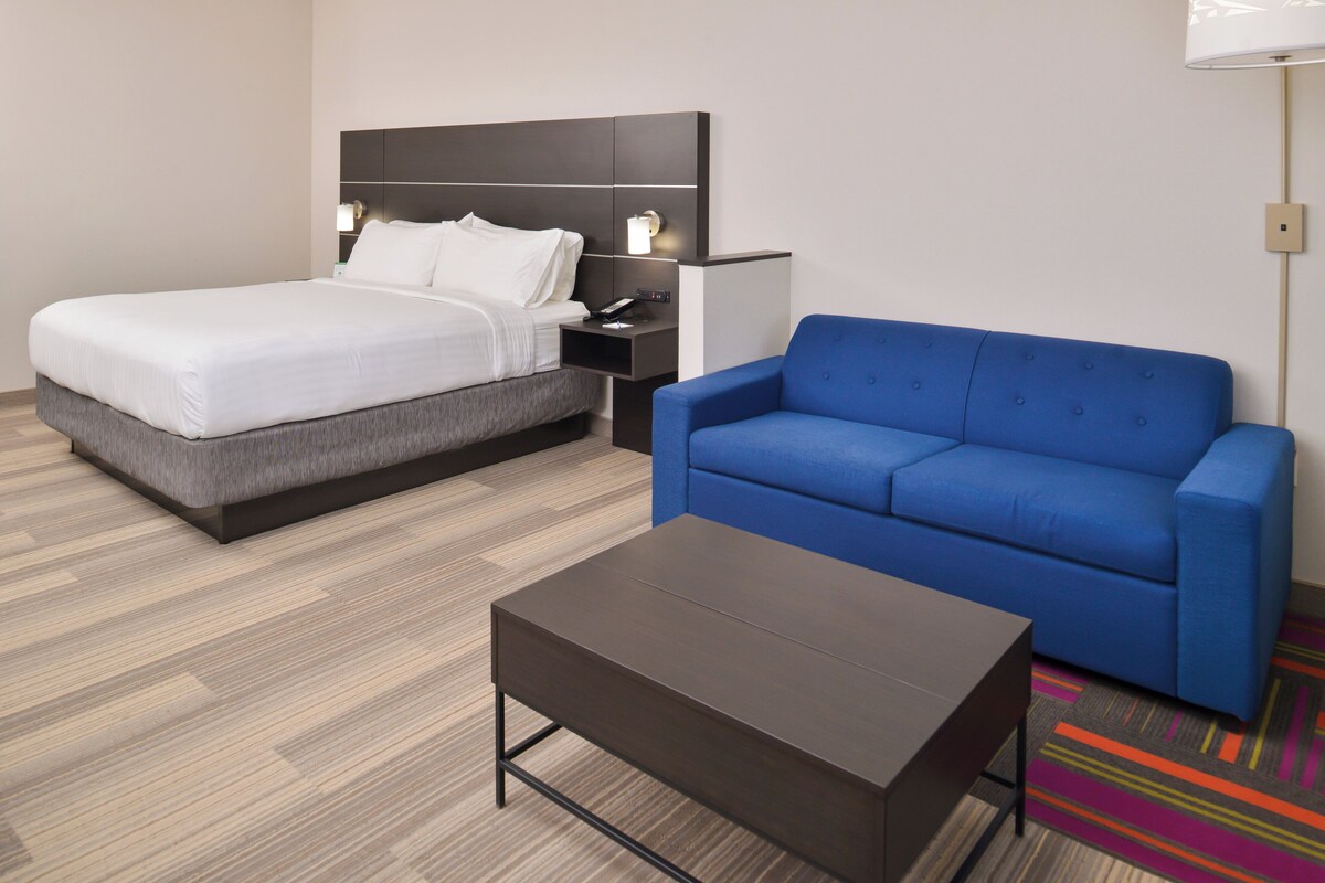Una habitación de hotel con una cama, un sofá azul, una mesa de centro y una mesita de noche con lámpara.