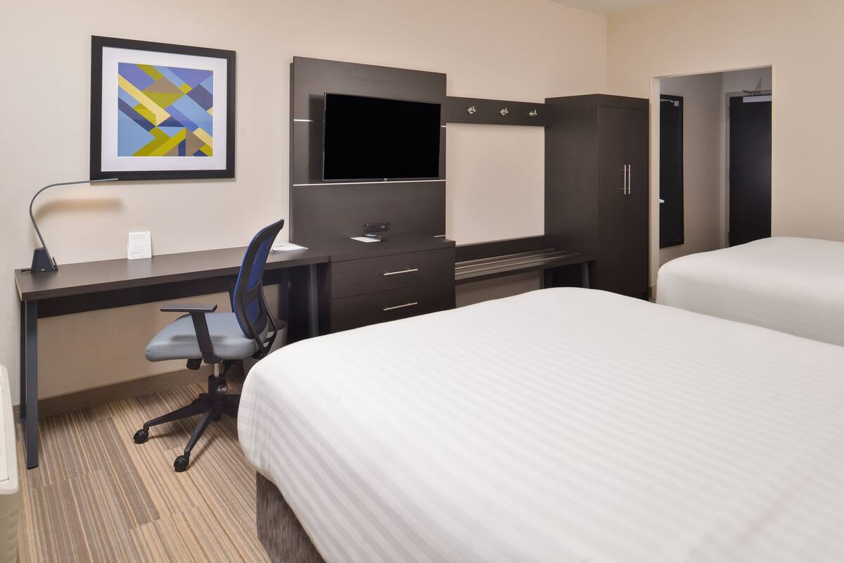 A hotel room with a bed, a desk with a chair, a television, and a wardrobe.