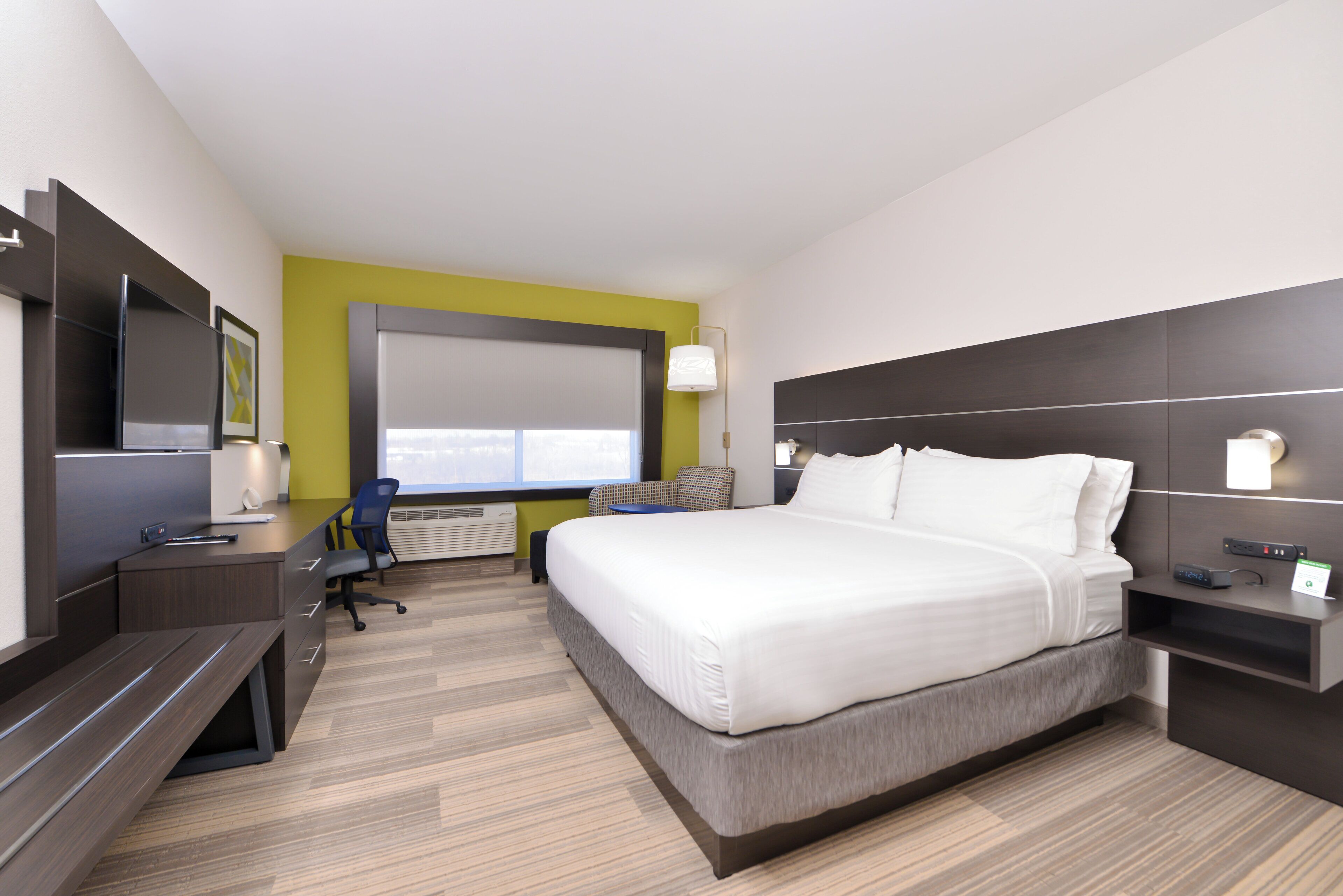 A modern hotel room with a bed, desk, chair, and a large window.