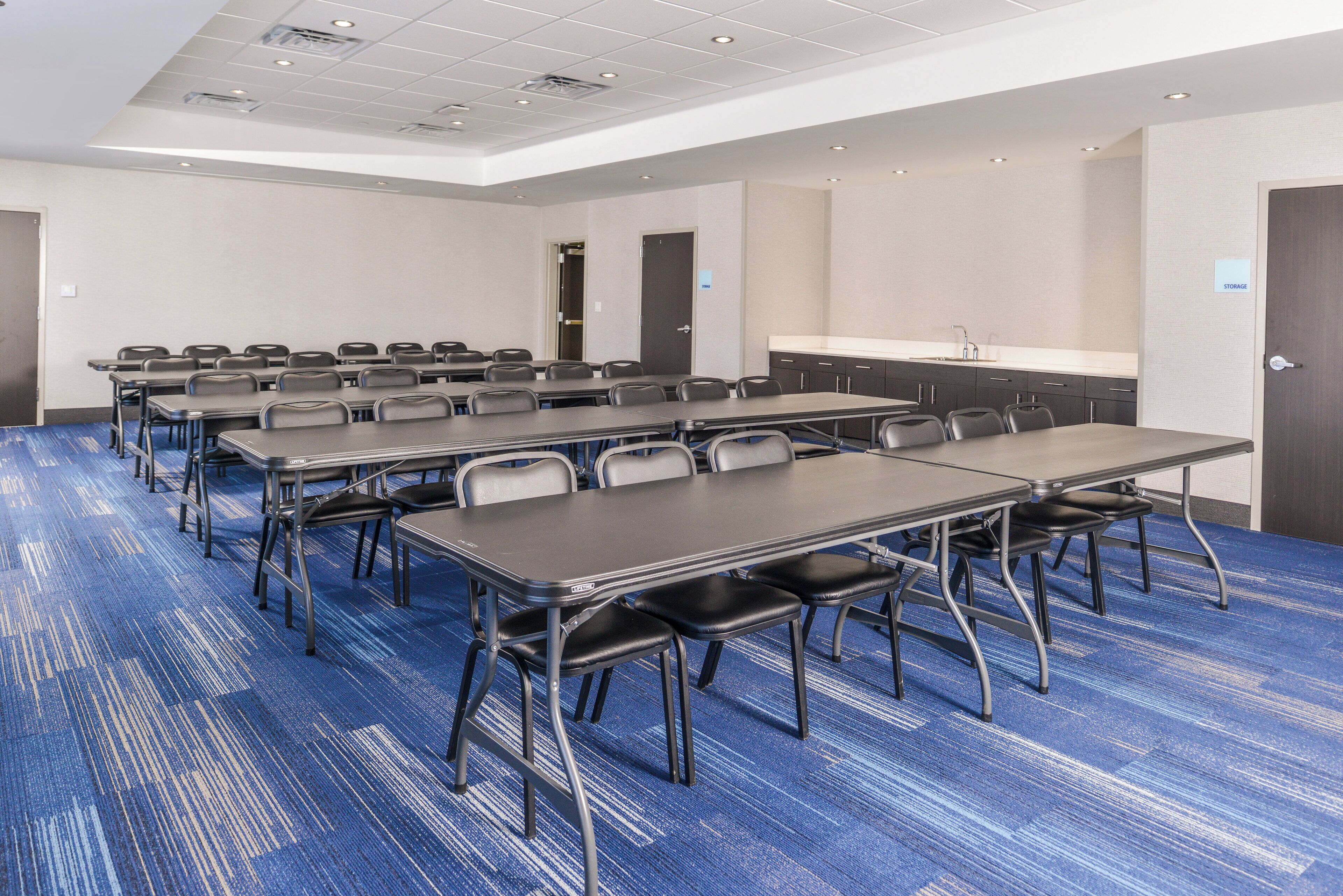 A conference room with multiple tables and chairs, a kitchenette, and a storage area.