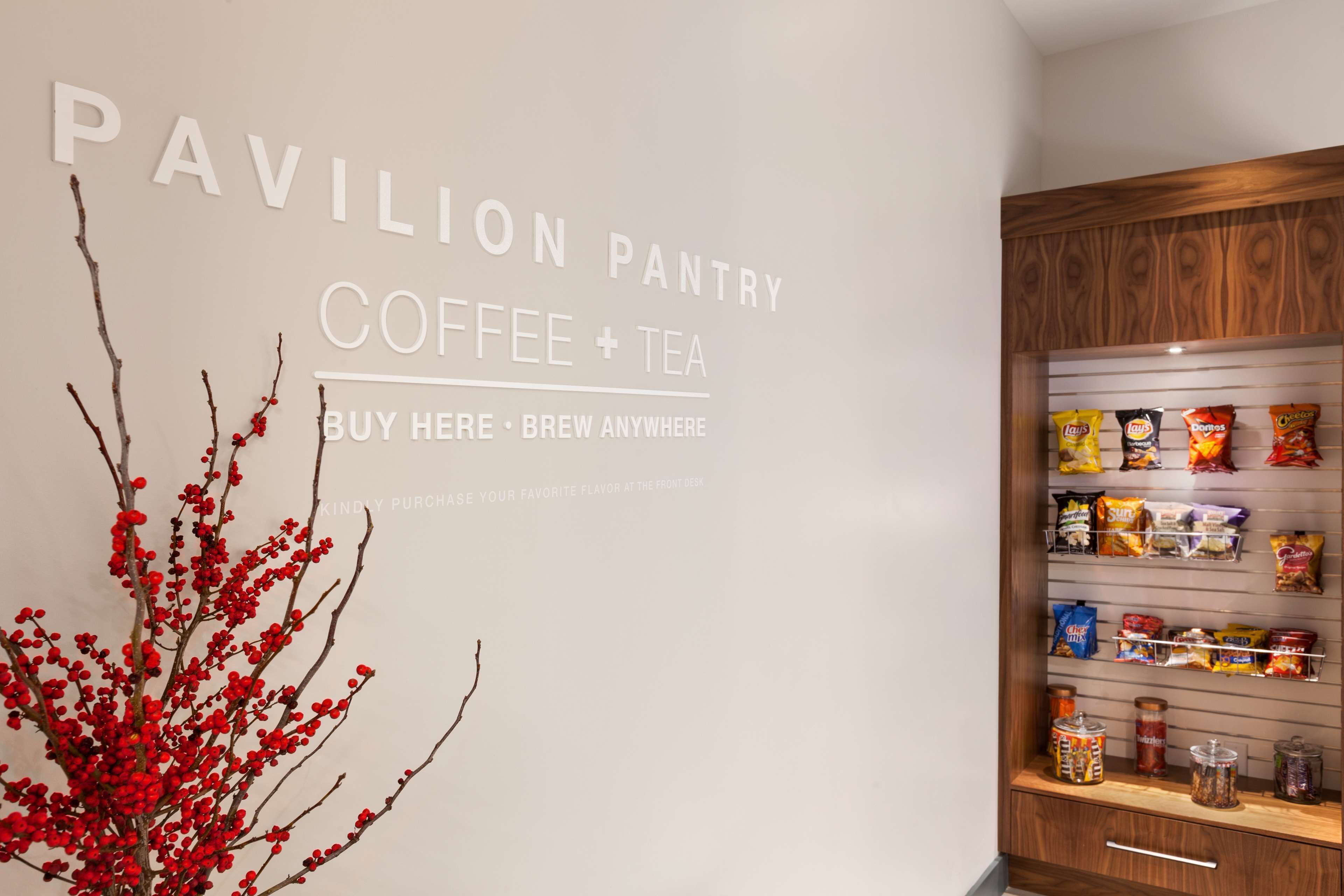 Una pared con letrero que dice 'Pavilion Pantry Coffee + Tea' y un estante de madera lleno de refrigerios.