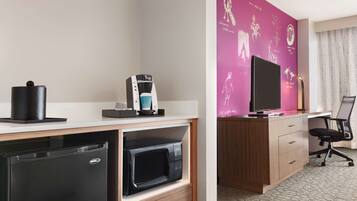 A compact hotel room with a kitchenette, a flat-screen TV, a desk, and a chair.