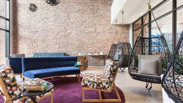 Een moderne zithoek met een bakstenen muur, een blauwe bank, gestreept fauteuils en een hangstoel.