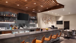 A modern bar area with a long counter, bar stools, and a variety of bottles and glasses. - Hilton Garden Inn Boulder (Boulder)