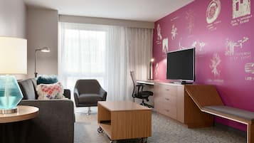 Una habitación de hotel moderna con un sofá gris, un escritorio de madera pequeño, un televisor y una pared con citas motivacionales.