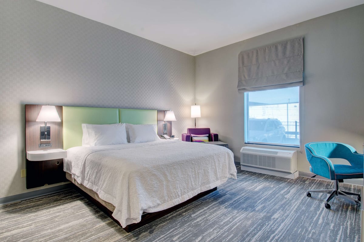 Une chambre d’hôtel avec un lit, des lampes de chevet, une chaise, une fenêtre et un radiateur.