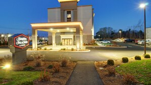 A modern hotel with a well-lit entrance, a visible parking area, and a signboard. - Hampton Inn & Suites Boston/Stoughton (Stoughton)