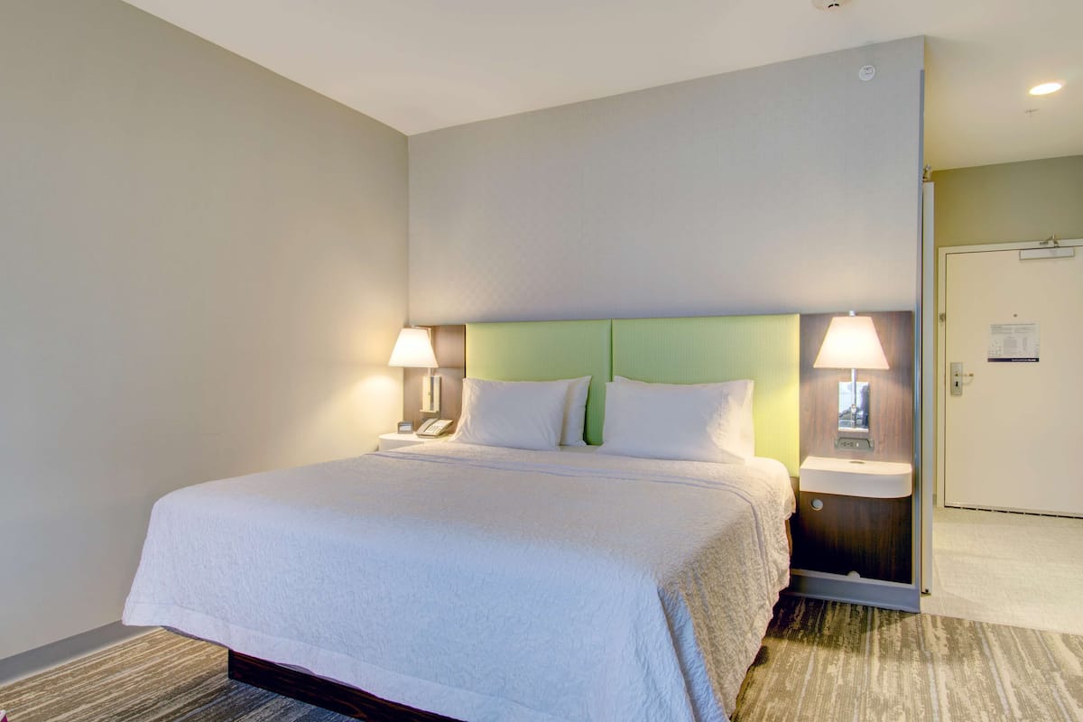 Une chambre d’hôtel avec un grand lit, deux lampes de chevet, une table de chevet avec un téléphone et un panneau de commande fixé au mur.