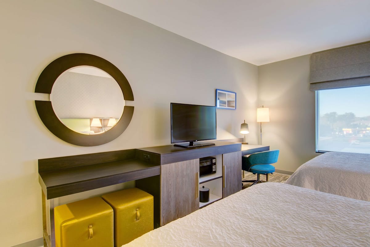 Une chambre d’hôtel avec un lit, une télévision, un bureau avec une lampe, une chaise et un miroir rond.