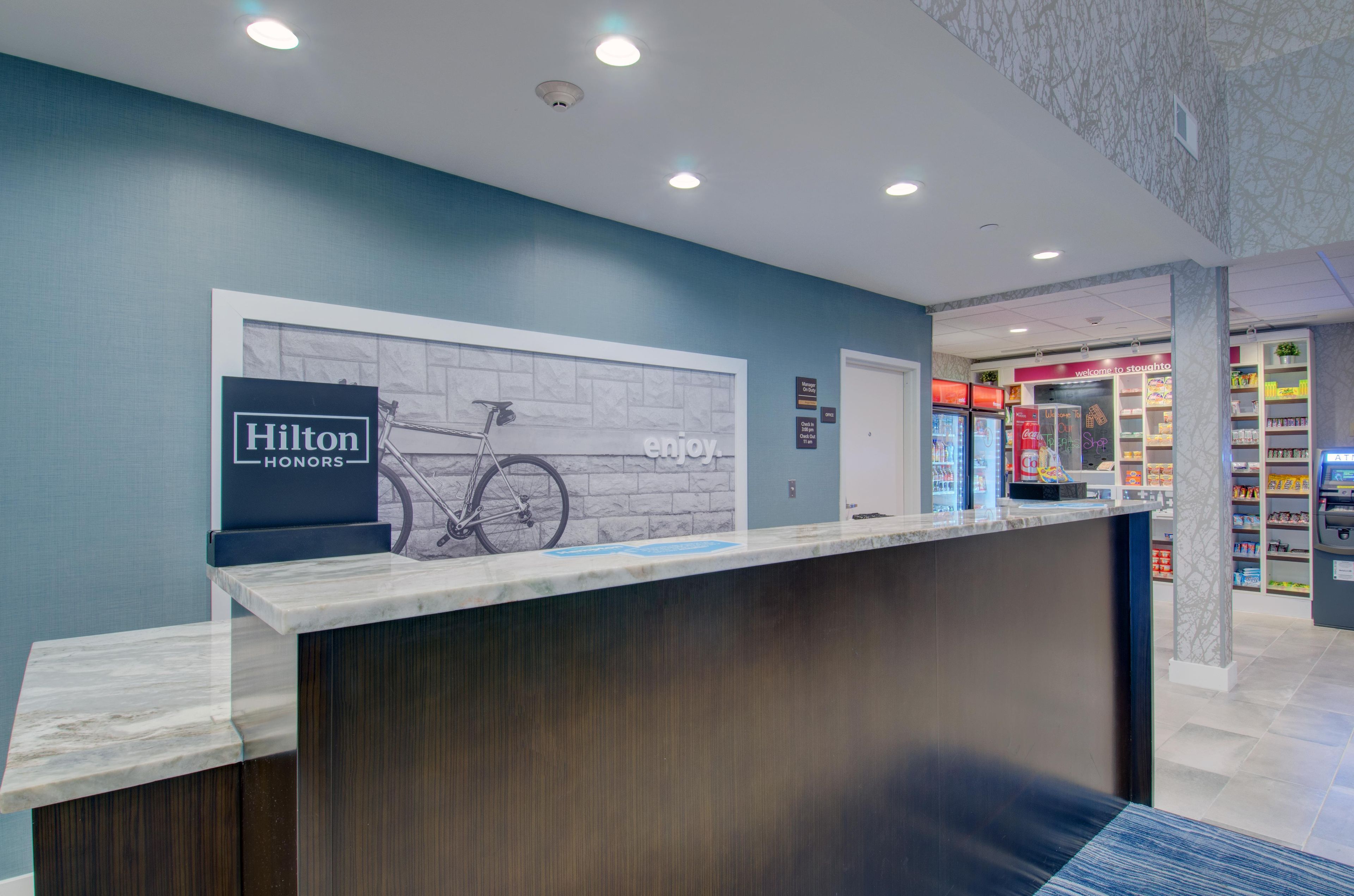 A hotel reception desk with a sign for Hilton Honors, a bicycle illustration, and a wall with the word 'enjoy'.