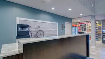 A hotel reception desk with a sign for Hilton Honors, a bicycle illustration, and a wall with the word 'enjoy'.