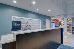 A hotel reception desk with a sign for Hilton Honors, a bicycle illustration, and a wall with the word 'enjoy'. - Hampton Inn & Suites Boston/Stoughton (Stoughton)